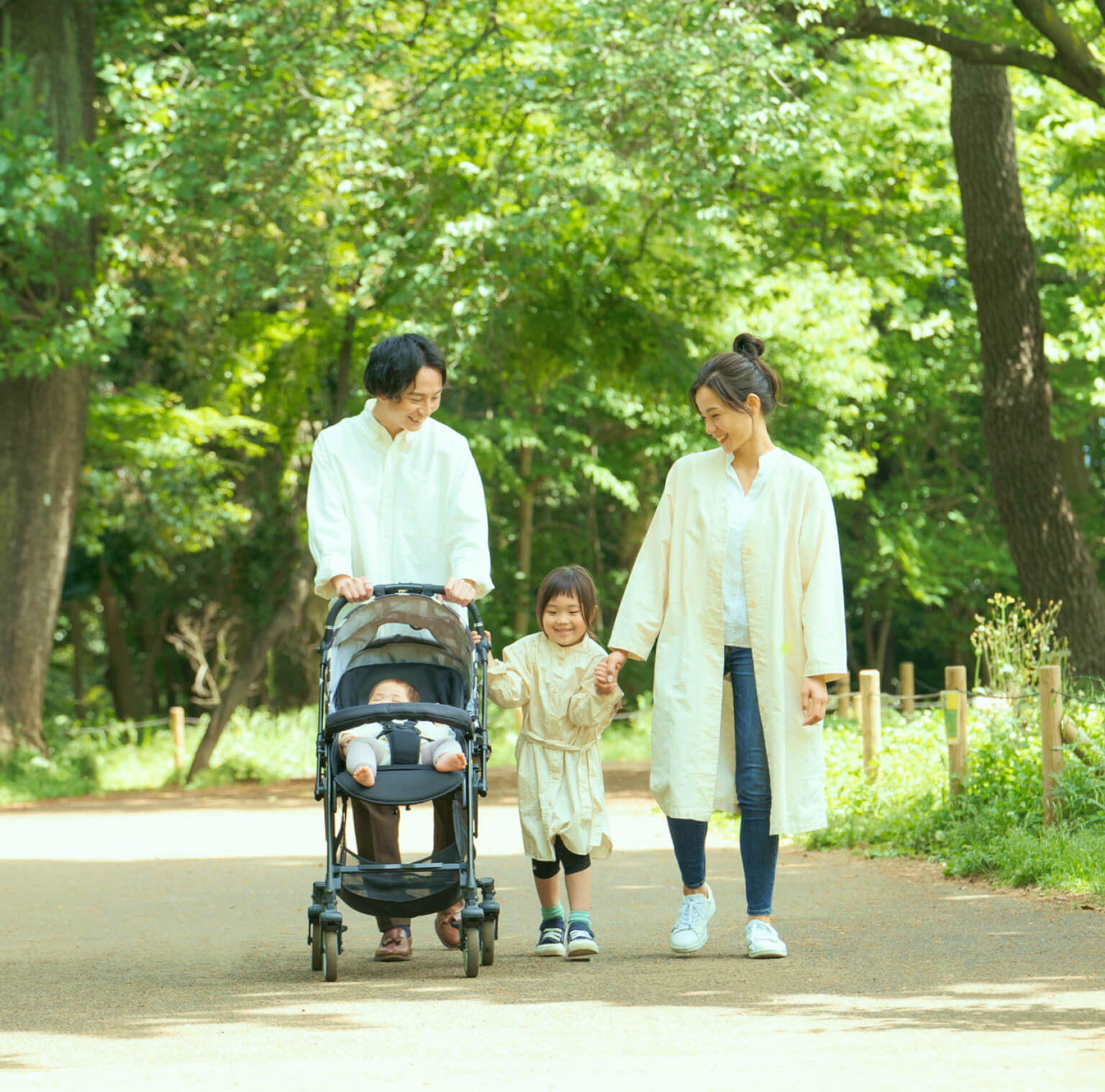 家族で散歩している。父親がベビーカーを押し母親と子どもが手を繋いでいる。
