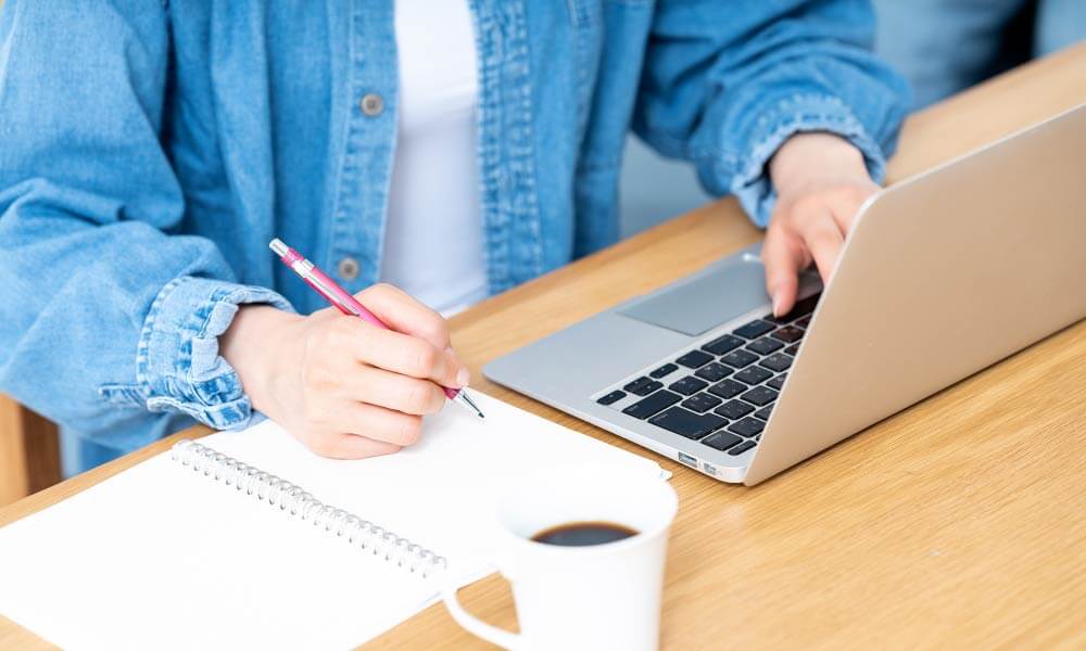 パソコンとノートを開き、ペンを持って勉強している
