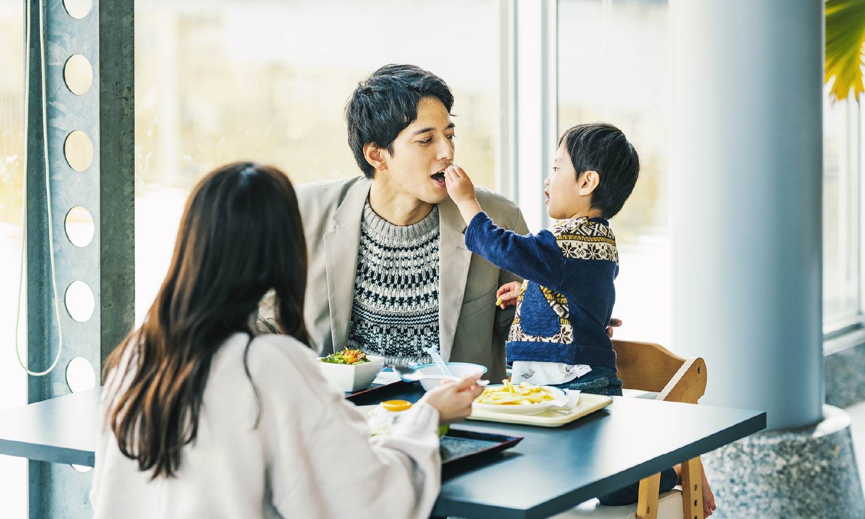 家族で食事をしている（子どもが父親の口に食べ物を入れている）